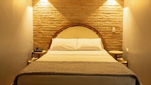 A hotel room with a brick wall, a wooden headboard, a bed with white linens, two bedside tables with lamps, and a telephone on one table. - Hotel El Arroyo (Caracas)