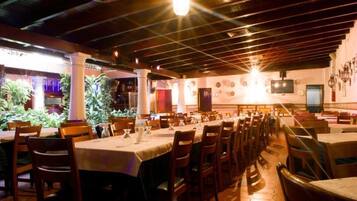 A restaurant with multiple tables and chairs, a tiled floor, and a ceiling with exposed beams.