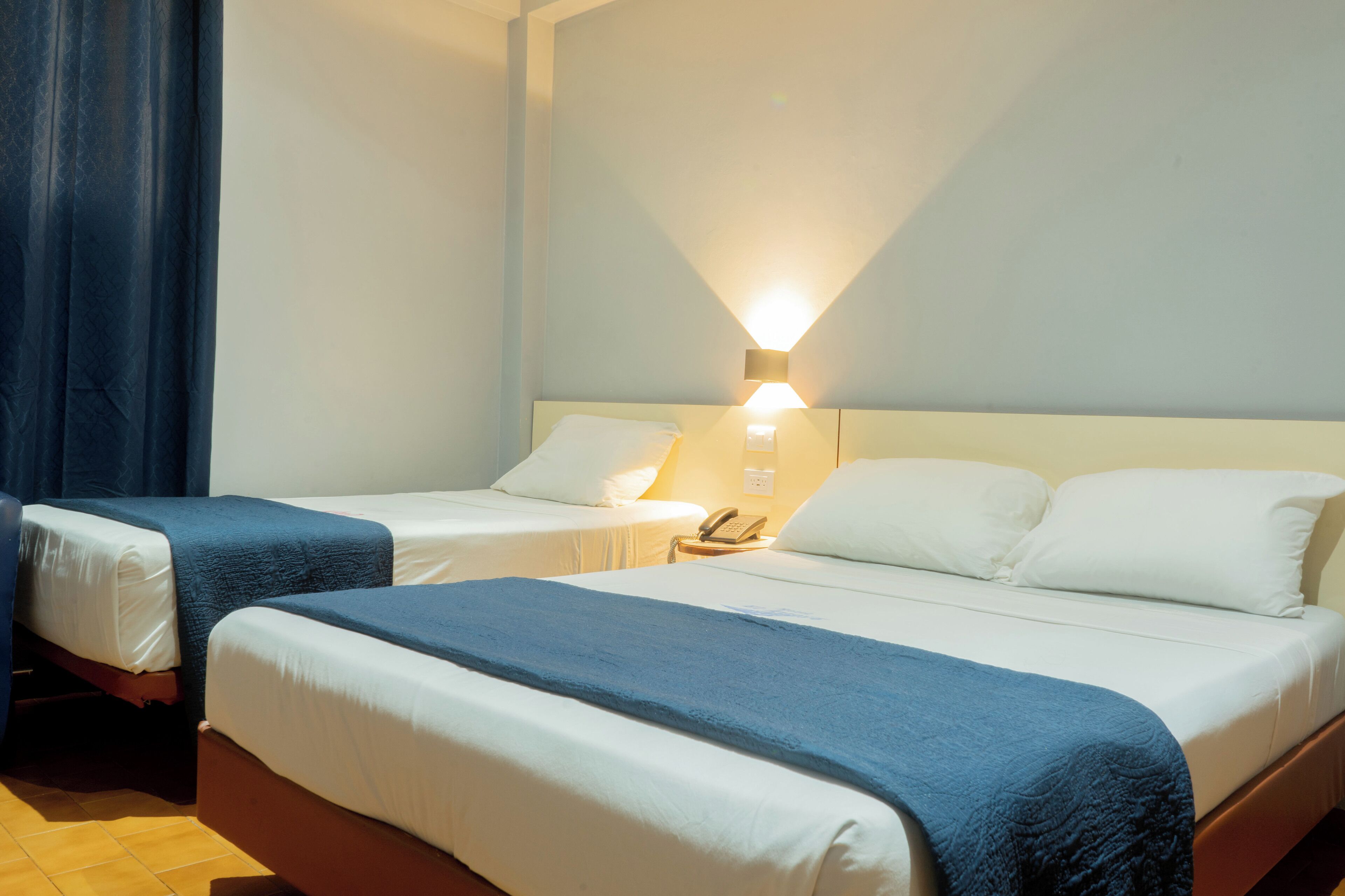 Une chambre d’hôtel avec deux lits, une table de chevet avec un téléphone et une lampe fixée au mur.