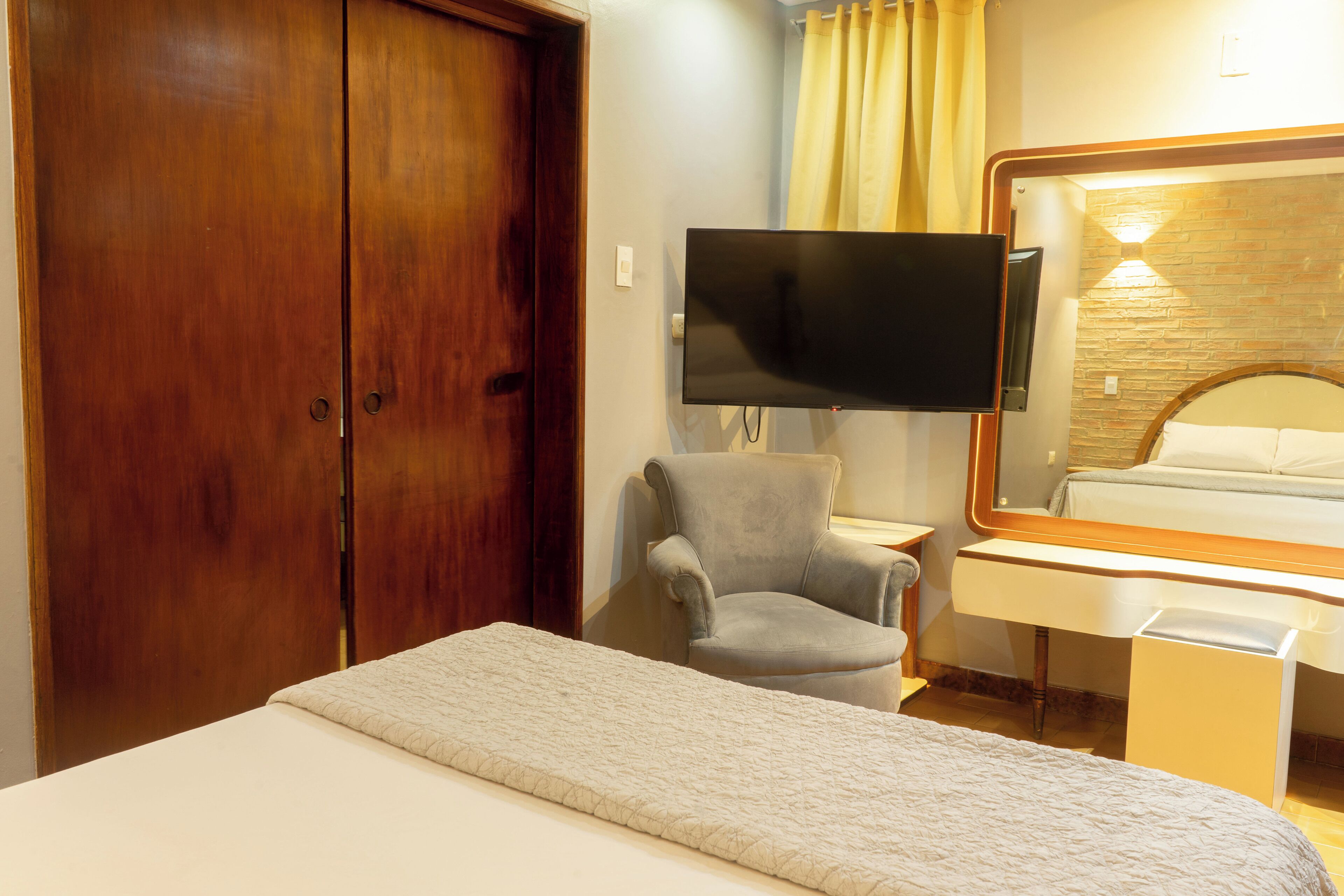 A hotel room with a bed, a desk, a chair, a TV, and a wardrobe.