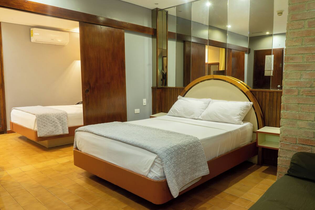 Een hotelkamer met twee bedden, een houten hoofdbord, een accentmuur van baksteen en een spiegel.