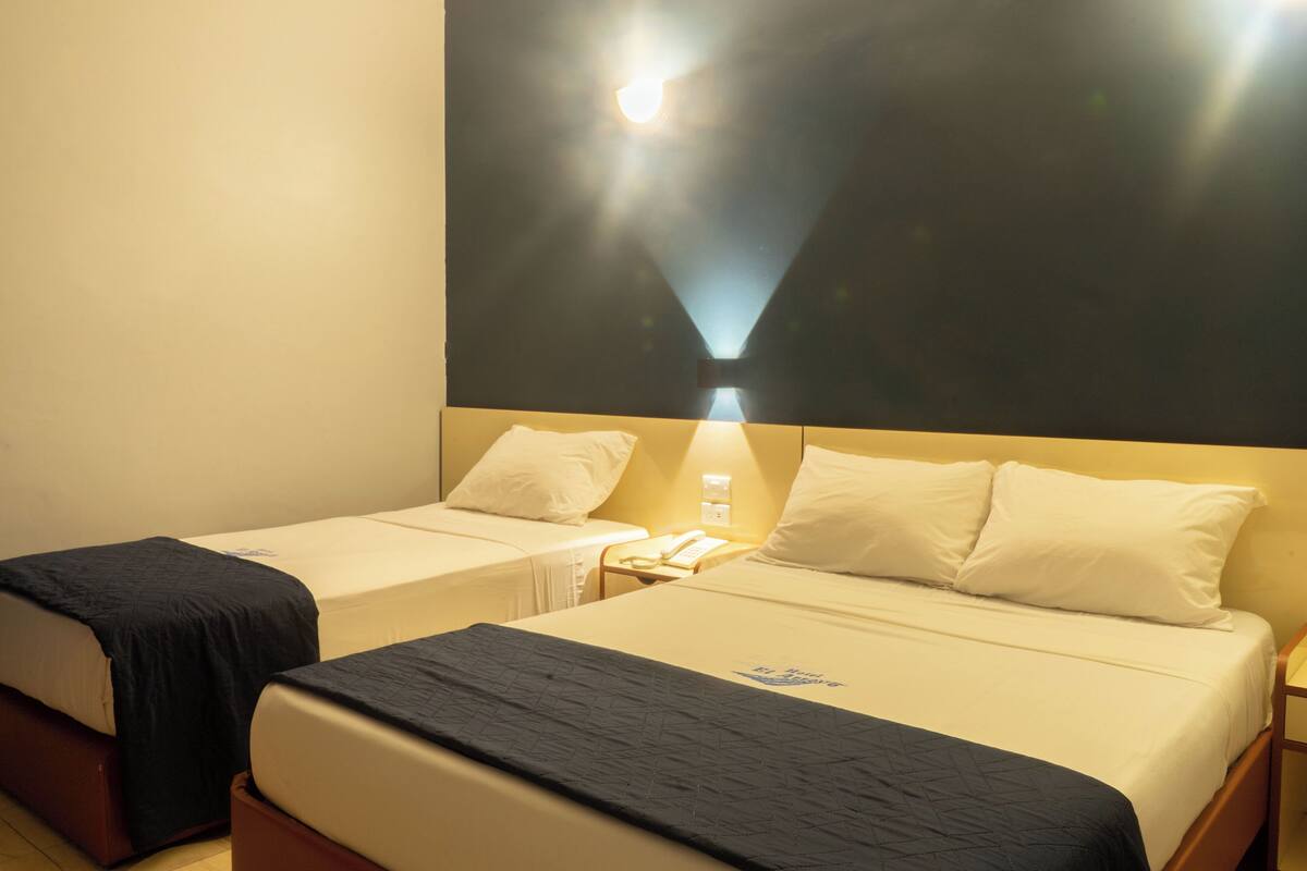 Een hotelkamer met twee éénpersoonsbedden, een nachtkastje met een lamp en een wandlamp.