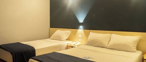 A hotel room with two single beds, a nightstand with a lamp, and a wall-mounted light fixture.