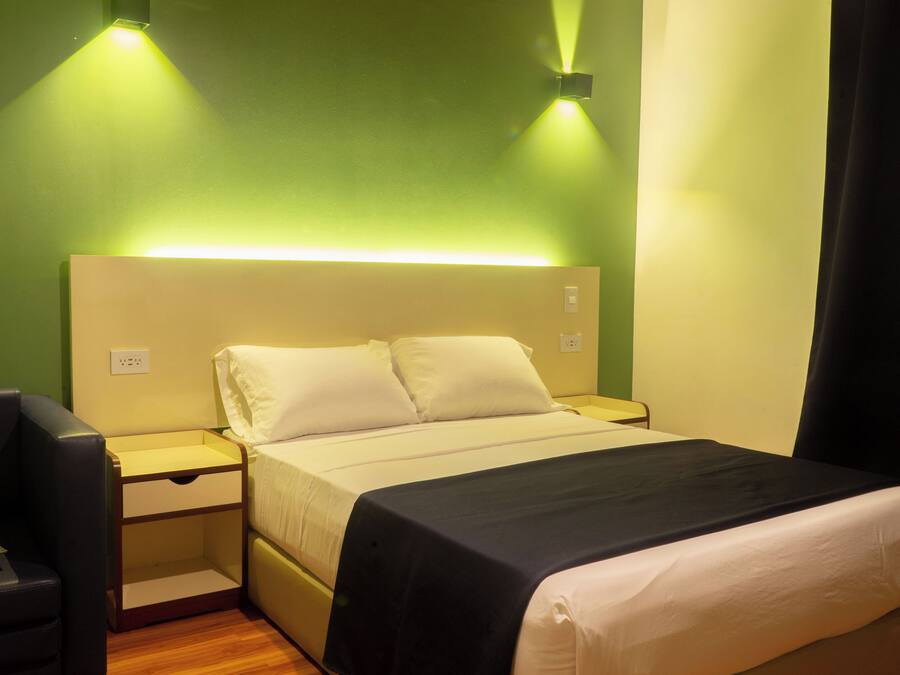 Una habitación de hotel con una cama, mesitas de noche, una silla y una mesita auxiliar.