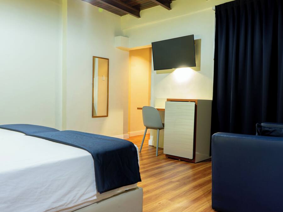 Habitación de hotel con cama, escritorio, silla, televisor y cortina oscura.