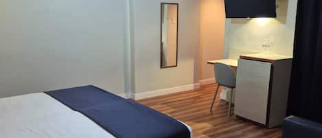 Una habitación de hotel con cama, escritorio, silla, televisor y espejo.