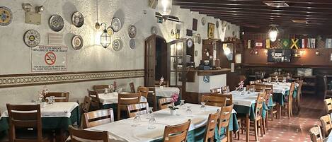 A restaurant with hexagonal patterned floor tiles, wooden chairs, and tables covered with white tablecloths.