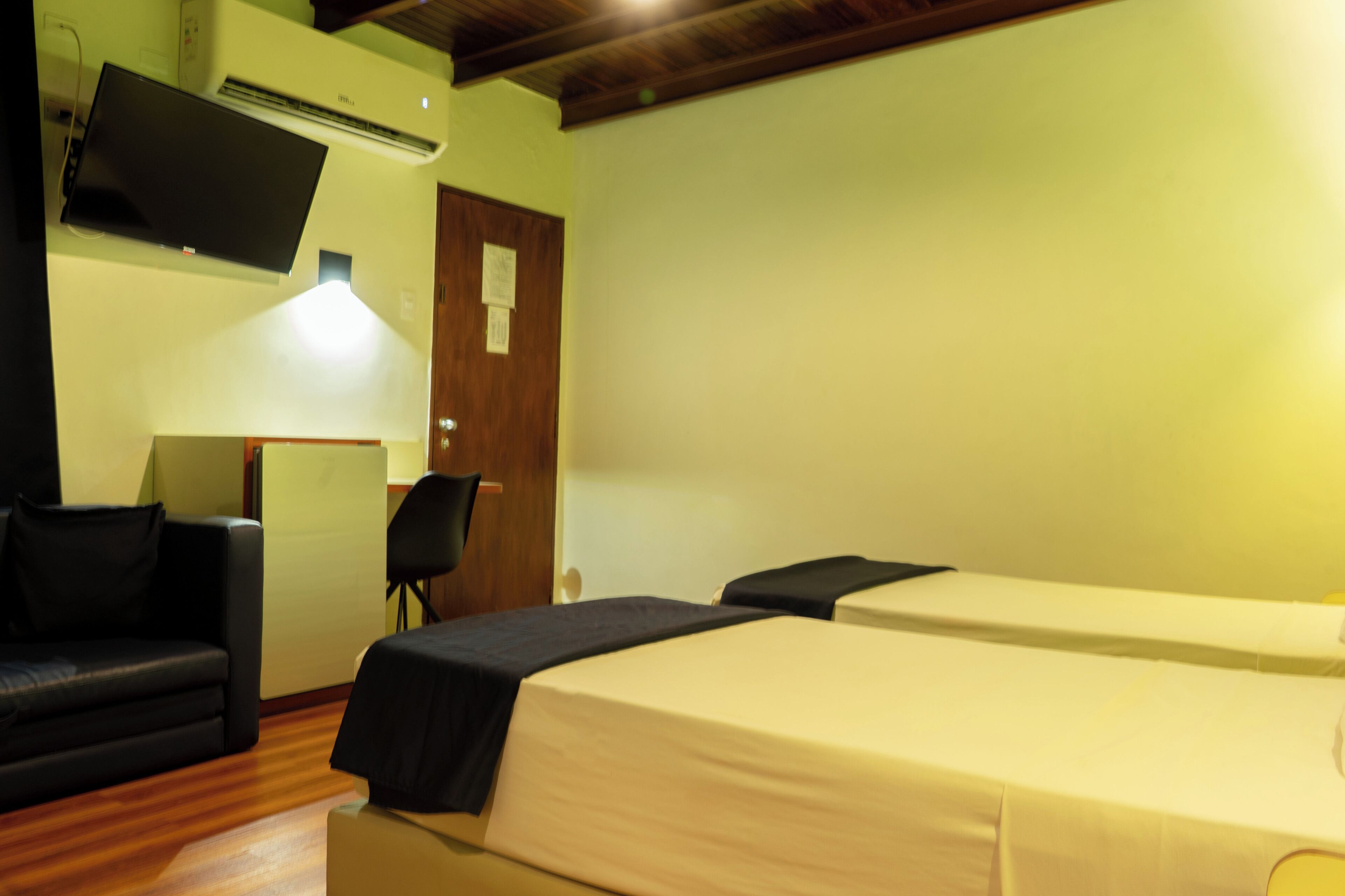 Une chambre d’hôtel équipée d’un lit, d’un canapé, d’un fauteuil et d’un téléviseur à écran plat fixé au mur.