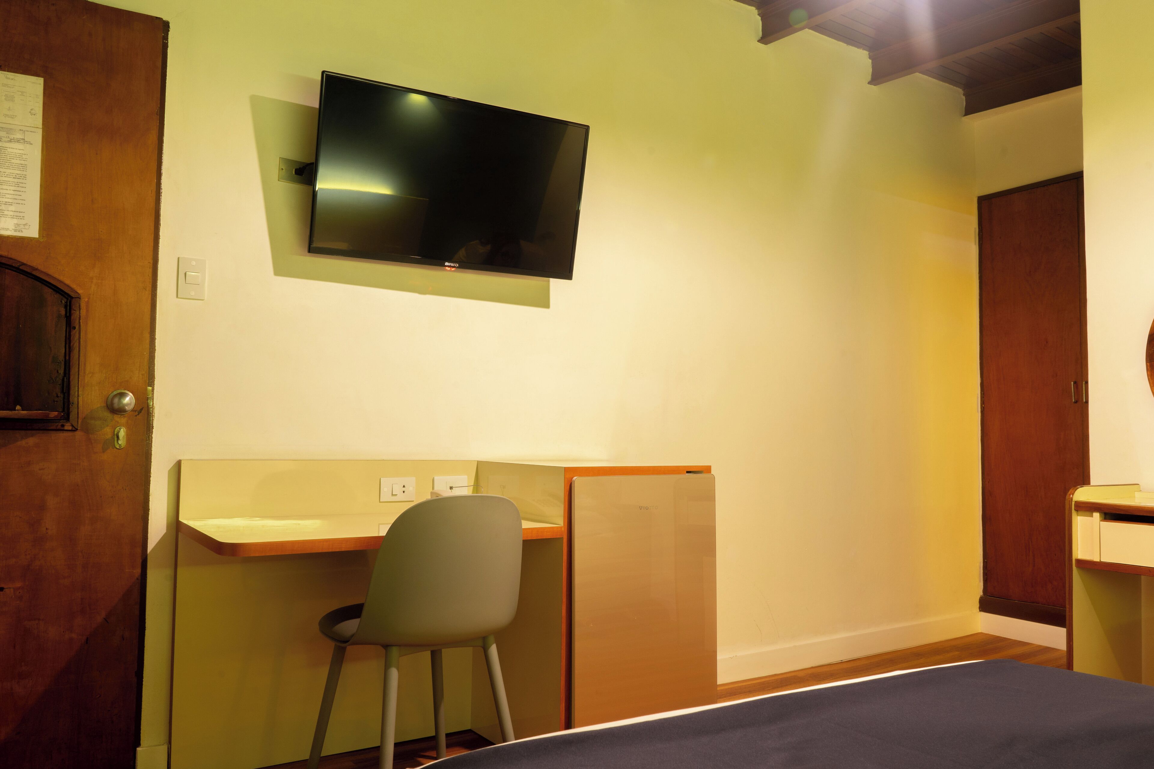 A room with a bed, a desk, a chair, a television mounted on the wall, and a door.