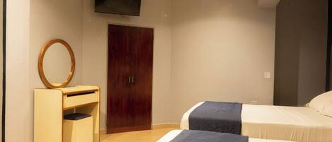 Habitación de hotel con dos camas, un armario de madera, un escritorio pequeño con espejo y un televisor en la pared.