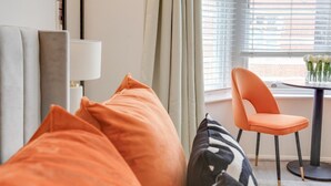 Una habitación de hotel moderna con una cama, una silla, una mesa con un jarrón de flores y una ventana con persianas.