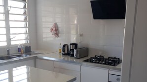 A modern kitchen with white cabinets, a stainless steel sink, a gas stove, and a toaster. - Source bis sea and hot water (Bouillante)