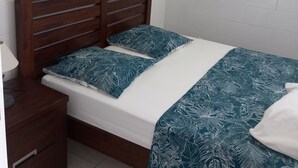 A bedroom with a wooden headboard, a white mattress, and a teal patterned bedspread. - Source bis sea and hot water (Bouillante)