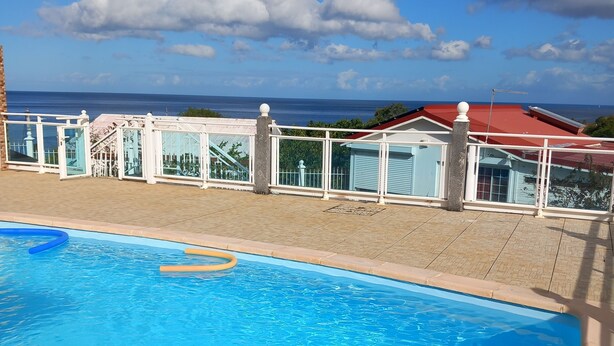 A swimming pool with a clear view of the ocean and a building with a red roof in the background. - Source bis sea and hot water (Bouillante)