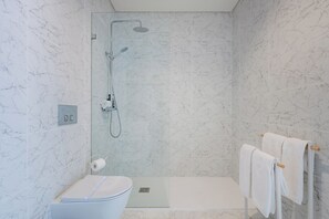 A modern bathroom with a glass-enclosed shower, marble walls, a toilet, and a towel rack. - Paraíso City Stay II (Porto)