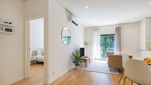 Una sala moderna con piso de madera, un espejo redondo, una planta en maceta y un comedor con sillas y una mesa.