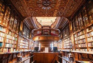 A library with ornate wooden ceilings, bookshelves, and a central staircase.
