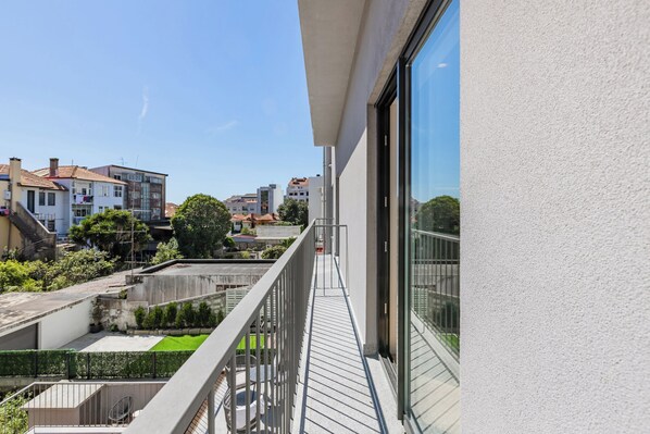 A modern building with a balcony overlooking a green courtyard and neighboring buildings.
