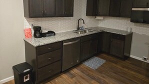 A kitchen with dark cabinets, a granite countertop, a stainless steel sink, and a coffee maker. - The Benjamin House, Quality and Comfortable Townhouse with small town feel (Hallsville)