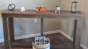 A wooden table with a woven basket underneath, a small potted plant, a decorative hourglass, and a cube-shaped object on the table. - The Benjamin House, Quality and Comfortable Townhouse with small town feel (Hallsville)