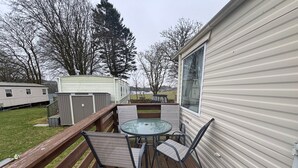 A deck with a glass table and chairs, a wooden fence, and a mobile home in the background. - No 38 Heilan Hoose at Three Lochs Newton Stewart (Newton Stewart)