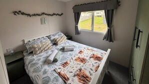 A bedroom with a bed, a window with curtains, a bedside table, and a wall-mounted decoration. - No 38 Heilan Hoose at Three Lochs Newton Stewart (Newton Stewart)