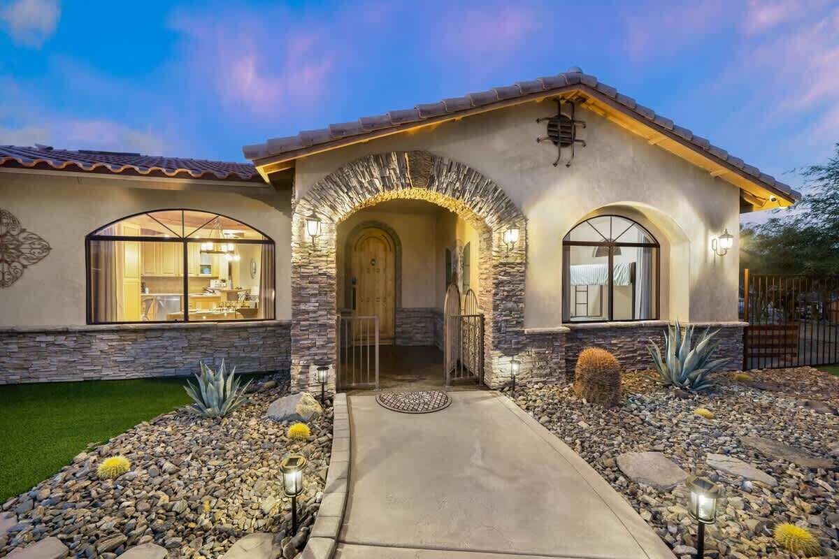 A residential building with a stone facade, arched entryway, and a landscaped front yard with cacti and rocks.
