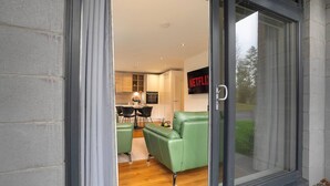 A modern living room with a green sofa, a dining area with a table and chairs, and a kitchen in the background.