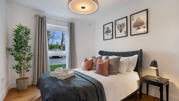 A bedroom with a bed, pillows, a bedside lamp, a plant, and a window with curtains.