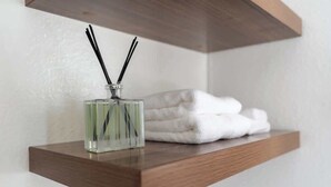 A wooden shelf with a glass bottle of reed diffuser and folded white towels. - Studio Hideaway in Beachwood (Los Angeles)