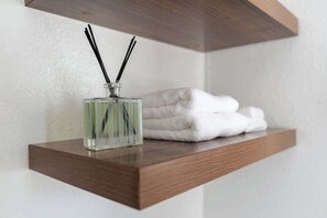 A wooden shelf with a glass bottle of reed diffuser and folded white towels.