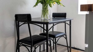 A small dining area with a table and two chairs, a vase with flowers, and a window. - Studio Hideaway in Beachwood (Los Angeles)