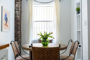 A dining area with a round table, two wicker chairs, a green vase with flowers, and a brick wall. - Urban Studio in Korea Town (Los Angeles)