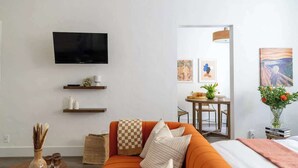 A modern living room with a sofa, a flat-screen TV, a small dining table, and a vase of flowers.