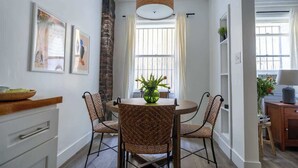 A dining area with a round table, wicker chairs, a hanging light fixture, and a window with curtains.