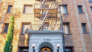 Un edificio a più piani in mattoni con una scala antincendio, una targa con il numero '1759' e un ingresso chiuso da un cancello.