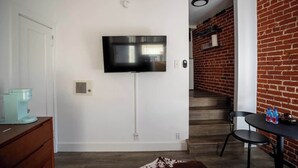 Un salon moderne avec un téléviseur à écran plat fixé au mur, une machine à café posée sur un meuble en bois et un escalier menant à un espace dont les murs sont en briques.