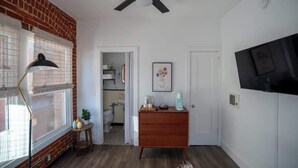 Une pièce dotée d’un ventilateur de plafond, d’une commode en bois, d’un téléviseur fixé au mur et d’une fenêtre avec des stores.
