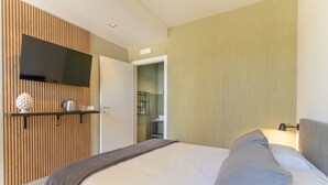 A modern hotel room with a large bed, a mounted TV, and a wooden panel wall.