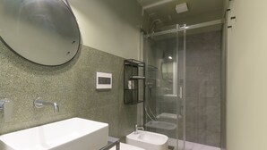 A modern bathroom with a large rectangular sink, a small pedestal sink, a glass-enclosed shower, and a wall-mounted mirror.