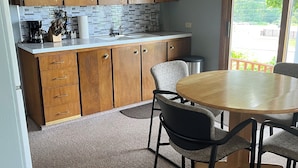 Une cuisine moderne avec des meubles de rangement en bois, un plan de travail et un coin repas comprenant une table ronde et des chaises.