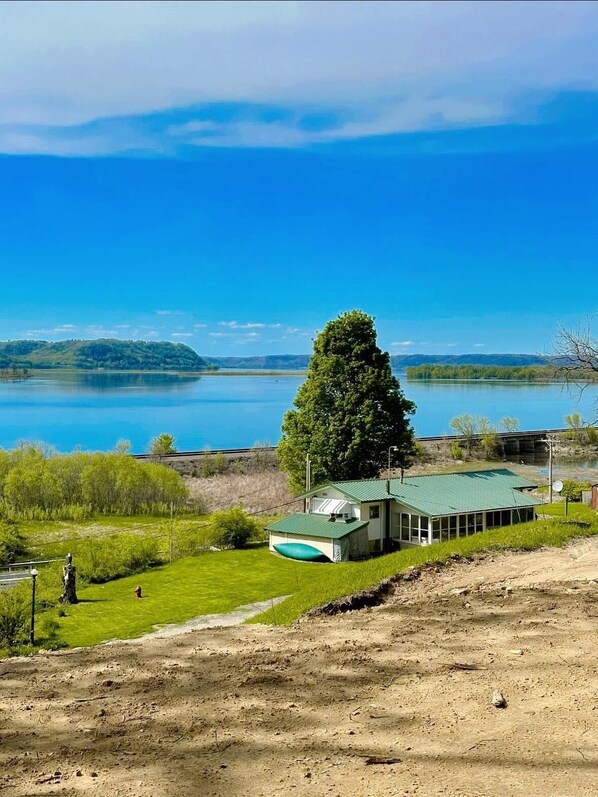 Una cabaña junto al lago con techo verde, rodeada de abundante vegetación y una vista despejada del lago.