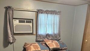 Une chambre à coucher avec un lit, une table de chevet, une fenêtre avec des rideaux et un appareil de climatisation fixé au mur.