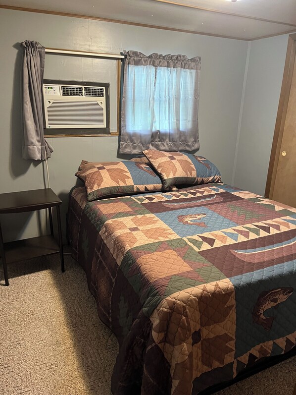 Un dormitorio con cama, mesita de noche, ventana con cortinas y un equipo de aire acondicionado en la pared.