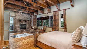 A bedroom with a stone fireplace, wooden beams, a large bed, and a view of the outdoors. - The Wildflower, Lodge+guest cabins 26 people (Alton)
