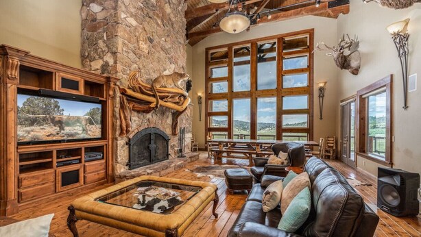 A rustic interior with a stone fireplace, leather furniture, and large windows offering a view. - The Wildflower, Lodge+guest cabins 26 people (Alton)