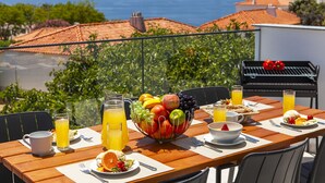 A dining table with a fruit bowl, breakfast items, and drinks, overlooking a scenic view of the sea and buildings. - Albufeira villa w/ heatable pool & sea views (Albufeira)