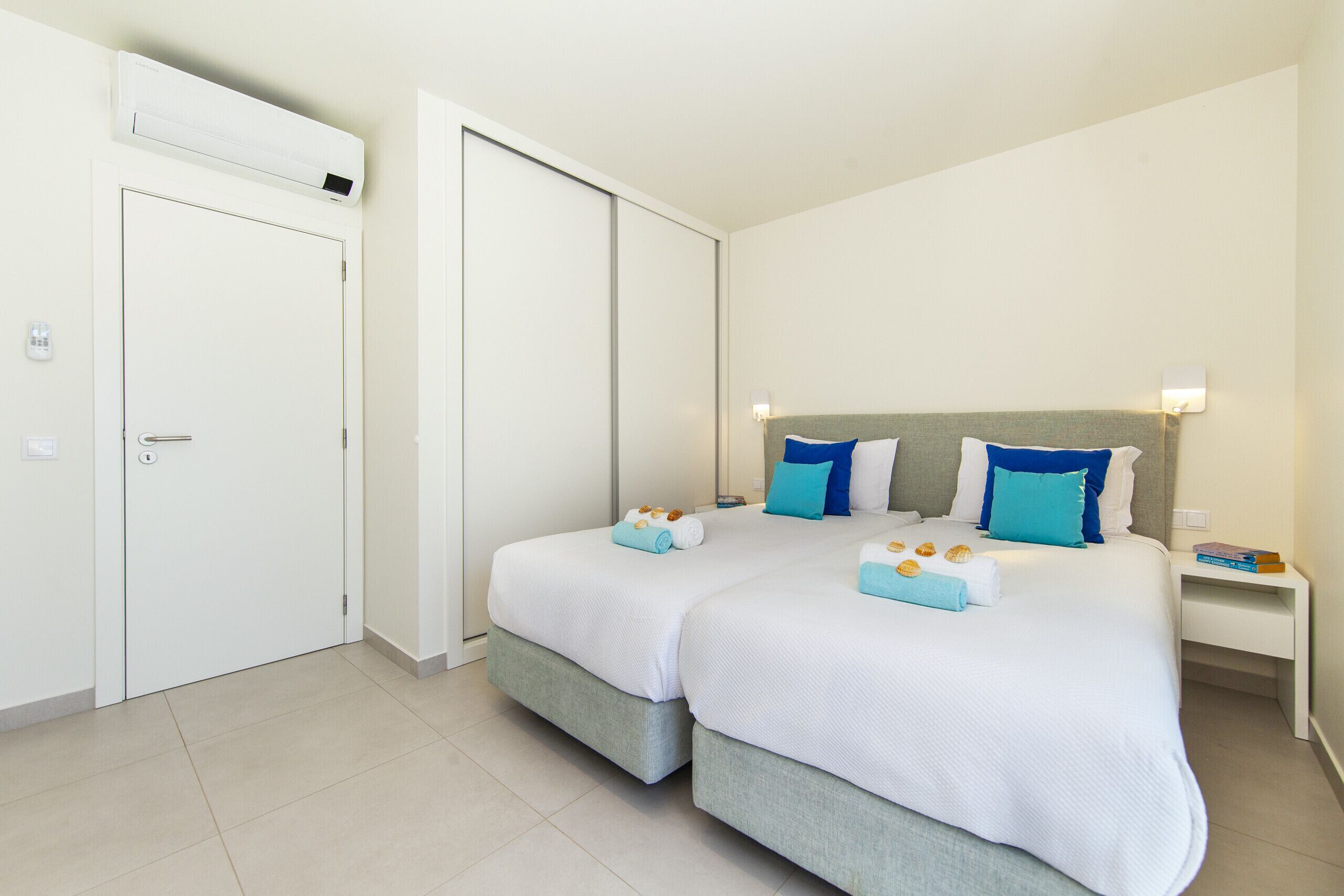 Una habitación de hotel con dos camas, un armario, una mesita de noche y un equipo de aire acondicionado.