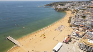 Vista aérea de un pueblo costero con una playa de arena, un muelle y edificios a lo largo de la costa.