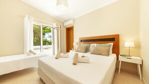 A hotel room with a large bed, a bedside table with a lamp, a window with curtains, and a view of greenery outside. - Cozy villa with heatable pool and BBQ (Carvoeiro)